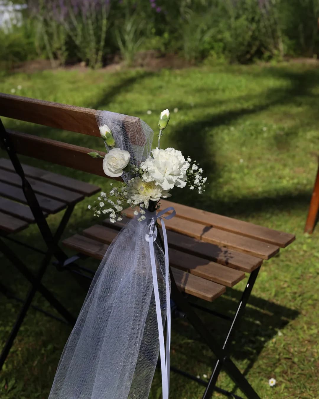 Folding chair by the aisle with falling tulle and a bouquet of white carnations and gypsophila, tied with a white ribbon