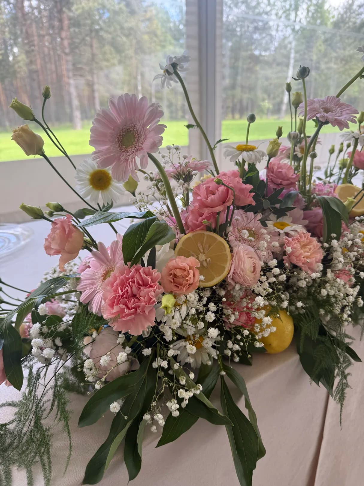 Close-up of an arrangement of pink gerberas, carnations, buttercups, chamomiles and gypsophila with a sliced lemon