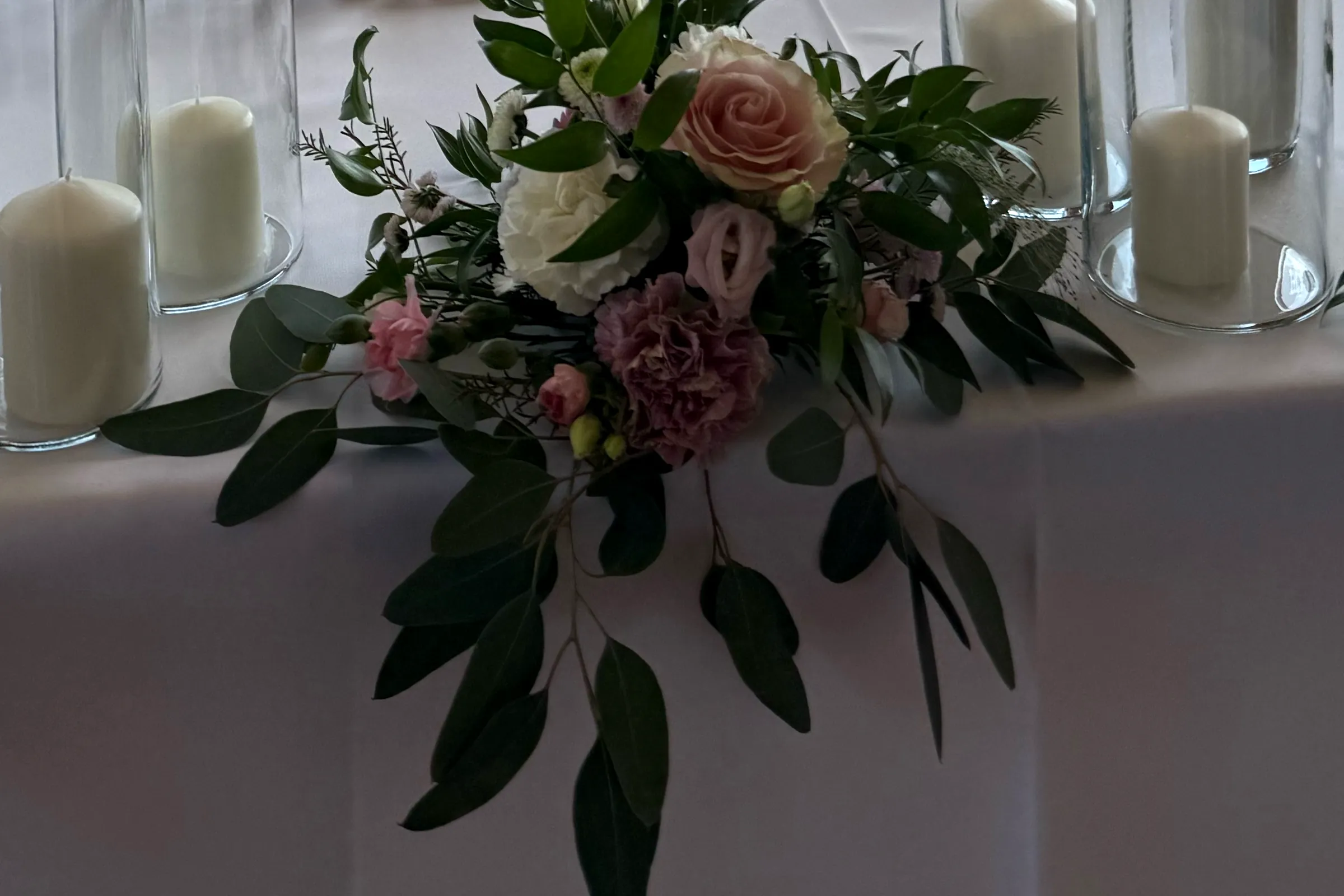 A garland of roses, carnations and eucalyptus flowing from the white tablecloth of the couple's table, candles in glass cylinders next to it