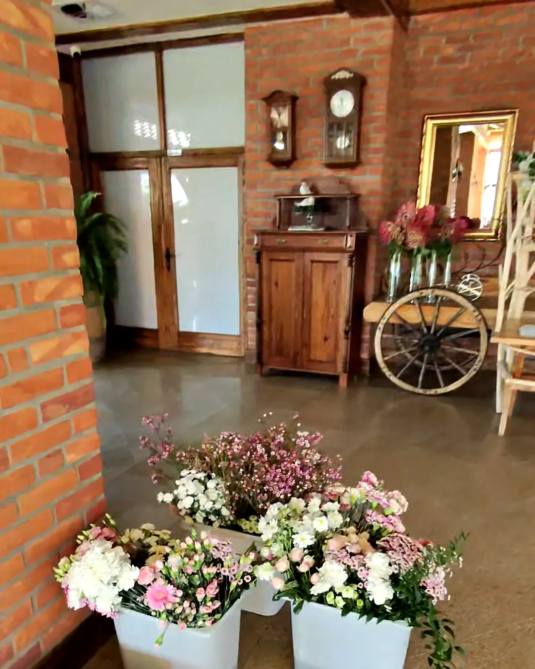 Buckets with carnations, gerbera and tiny pink flowers near a brick pillar, prepared for decoration installation
