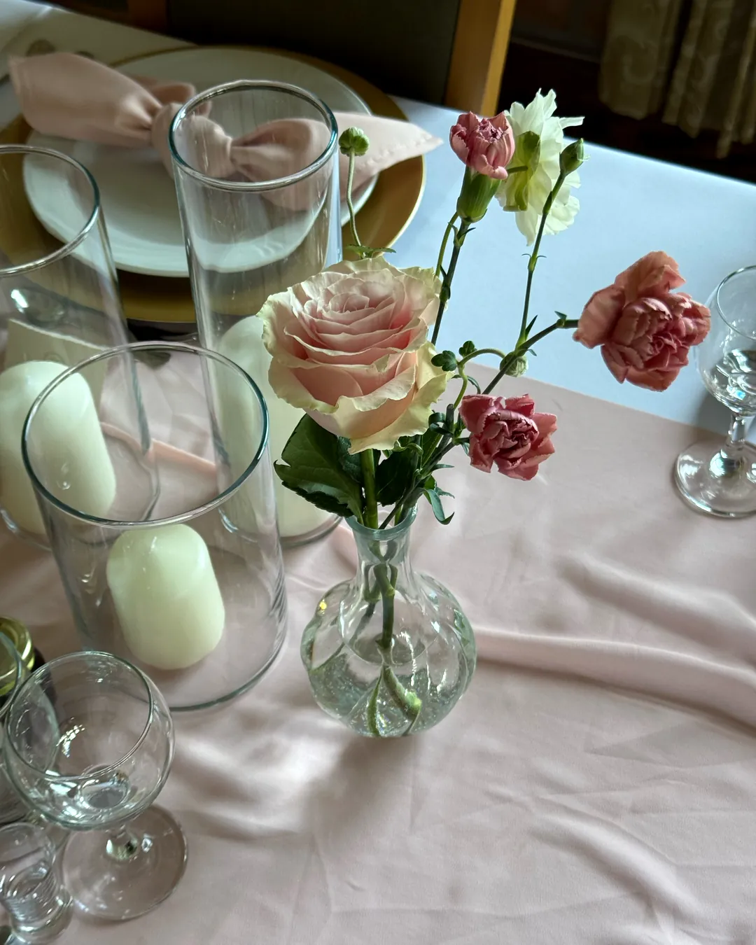 Powder rose and dark pink carnations in a glass vase next to white candles in glass cylinders