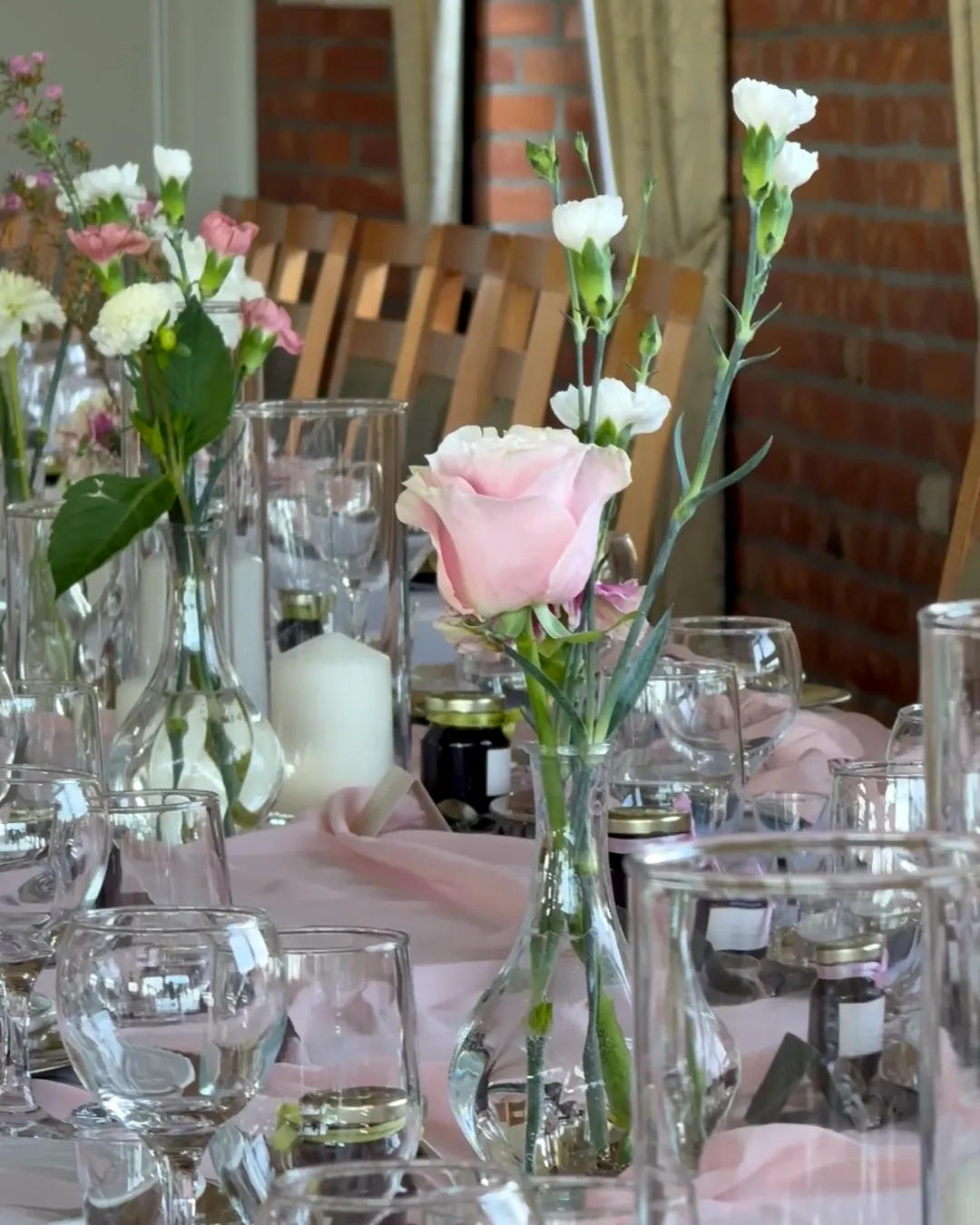 Pink rose and white carnations in a glass vase with a candle in the glass, on a table with a pink table runner