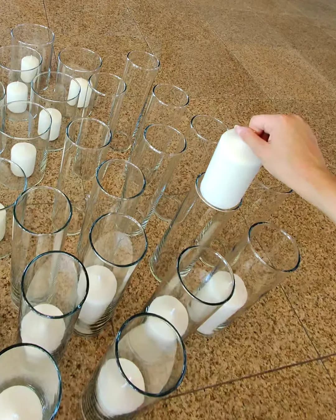 Glass cylinders with white candles placed on the floor before assembly, ready to be placed on the tables