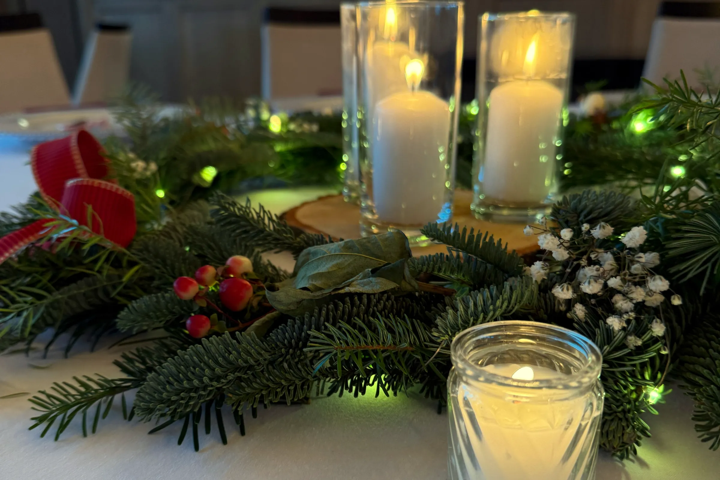 Candles in glass on a wood slice surrounded by fir, gypsophila and red fruits, in front a candle in a jar