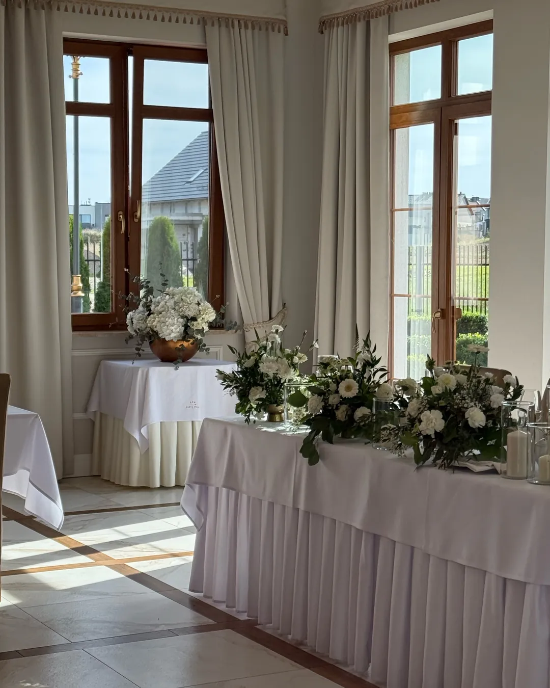 The bride and groom's table with white compositions in a bright corner of the room, next to it there is a round table with hydrangeas in a golden bowl