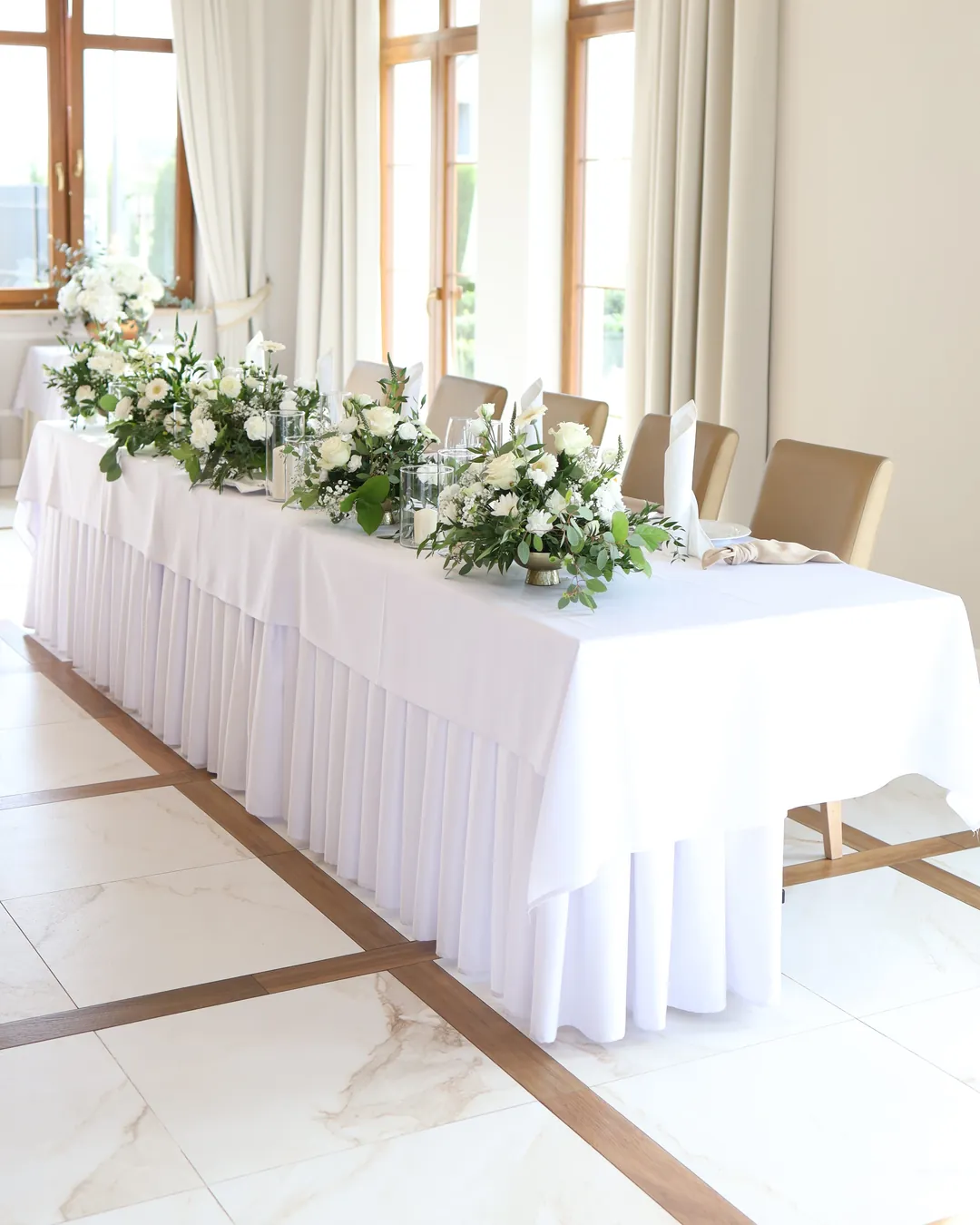 The bride and groom's table with a white tablecloth, low compositions of white flowers and napkins rolled into cones