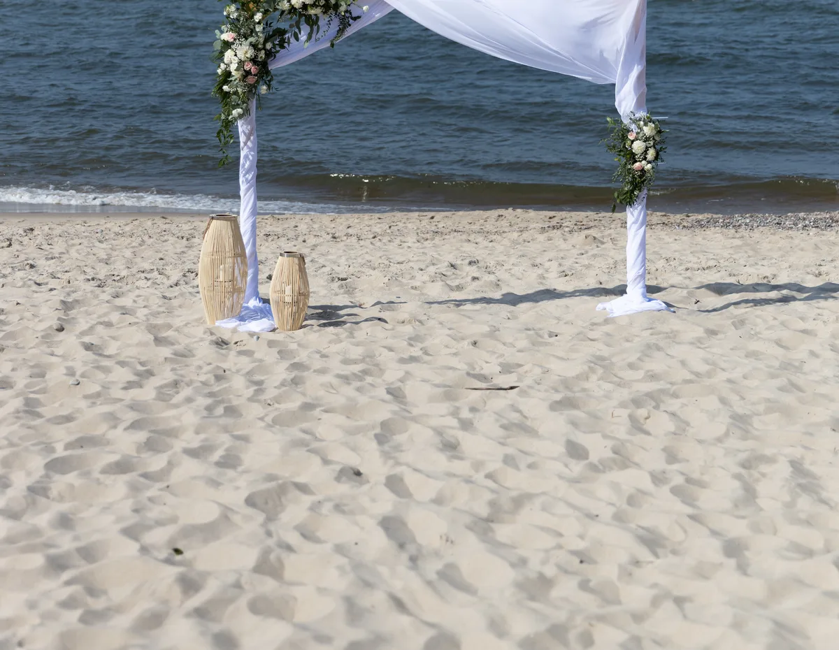 Łuk kwiatowy z draperią i zielenią na plaży podczas ceremonii ślubnej